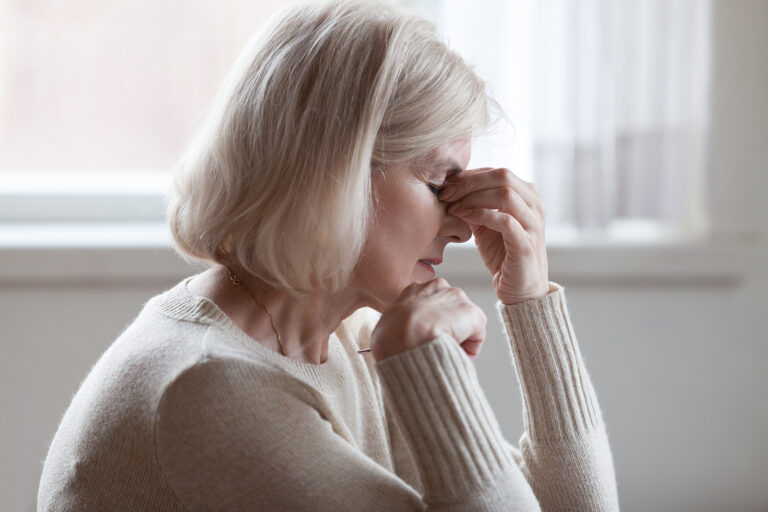 A senior woman pinches the bridge of her nose in discomfort