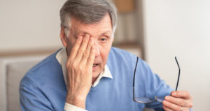 A senior man holds his glasses and rubs his eye