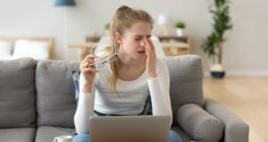 A young woman has taken her glasses off and is rubbing her eyes