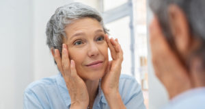 A senior woman touches her temples while looking at herself in the mirror