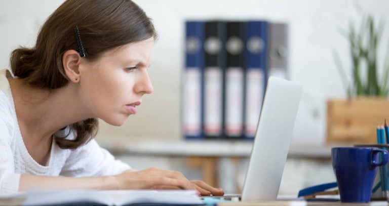 A woman squints her eyes while looking at her laptop screen.