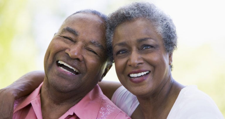 An older couple smiles joyfully at the camera.