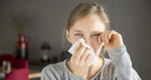 A young woman is crying and wiping her tears away with a tissue and her hand