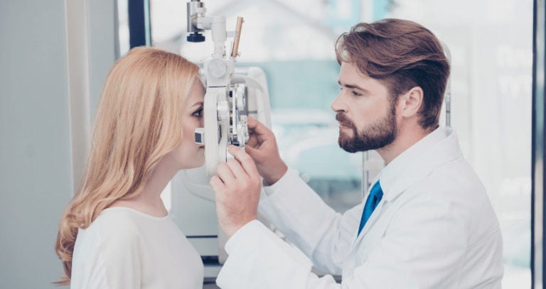 An eye doctor performs an eye exam on a female patient