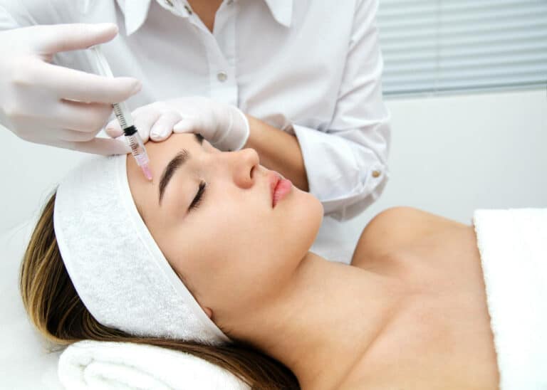 Doctor injects a patient as she lays on a bed with a towel wrapped around her head