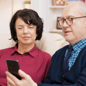 A man wearing glasses and a woman not wearing glasses look at the man's cellphone.