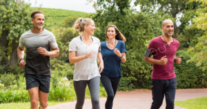 Two women and two men in athletic wear run alongside each other on a path outside. They are all smiling.