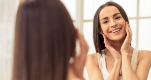 A young woman touches her face and smiles at herself in the mirror