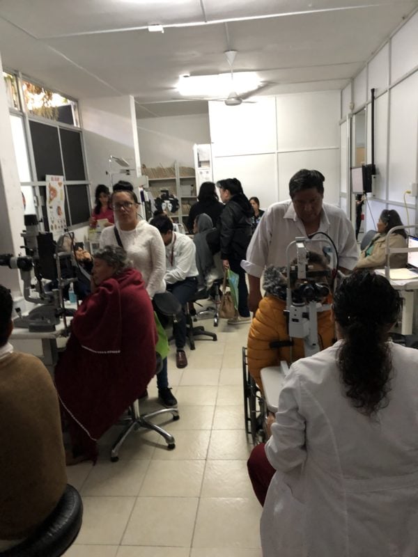 Various patients are seated and using eye-examining machines in Dr. Chokshi's mission trip exam room