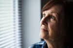 A senior woman looks out her window