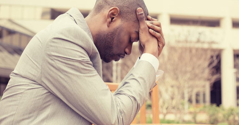 A young man holds his head tightly and closes his eyes