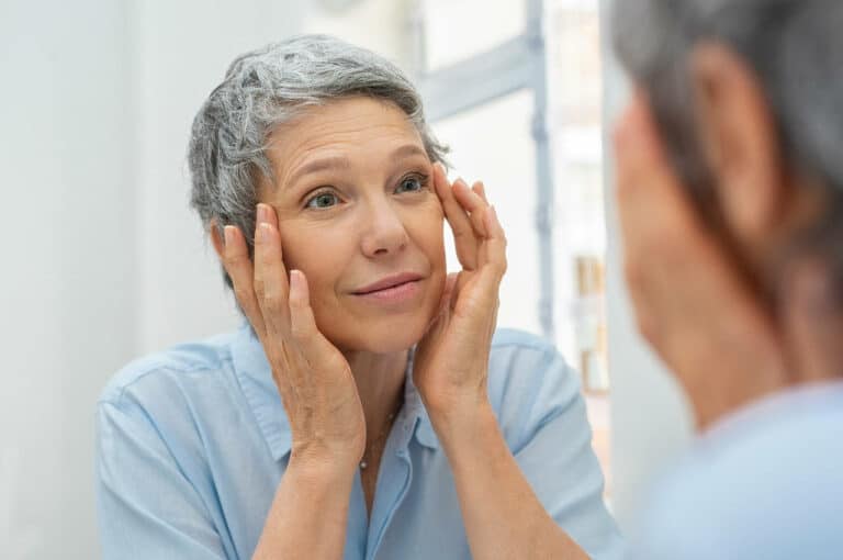 Woman looking into mirror and holding both of her hands up to her face