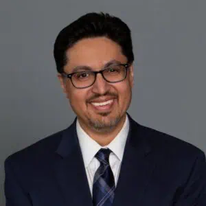 Headshot of Dr. S. Akbar Hasan in professional wear with a grey background.