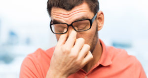 A man pushes his glasses up while he closes his eyes and pinches the bridge of his nose