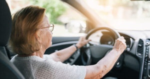 An older woman with glasses is holding her steering wheel while driving