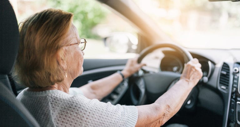 An older woman with glasses is holding her steering wheel while driving