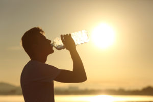 A man drinks from a large water bottle outdoors