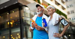 A senior couple holding water bottles and wearing athletic clothing are looking ahead