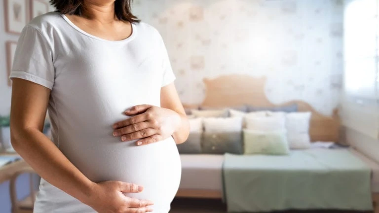 A woman holds her pregnant belly in a bedroom