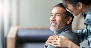 A woman puts her hands on the shoulders of an older smiling man