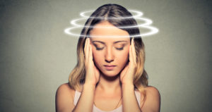 A young woman holds her head and closes her eyes. A graphic of three rings circles around her head indicating the types of ocular migraines