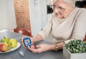 A senior woman checks her blood sugar with glucometer in the kitchen.