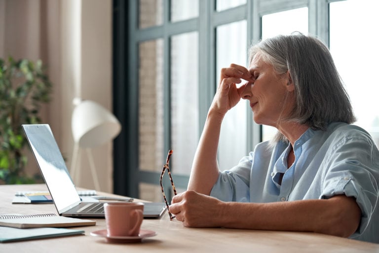 old woman with glasses in hand in front of computer rubbing eyes