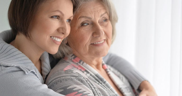 A woman hugs her mother and they both look out the window and smile.