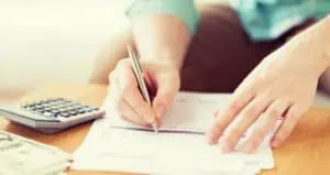 Someone writing on a piece of paper with a pen using a calculator.